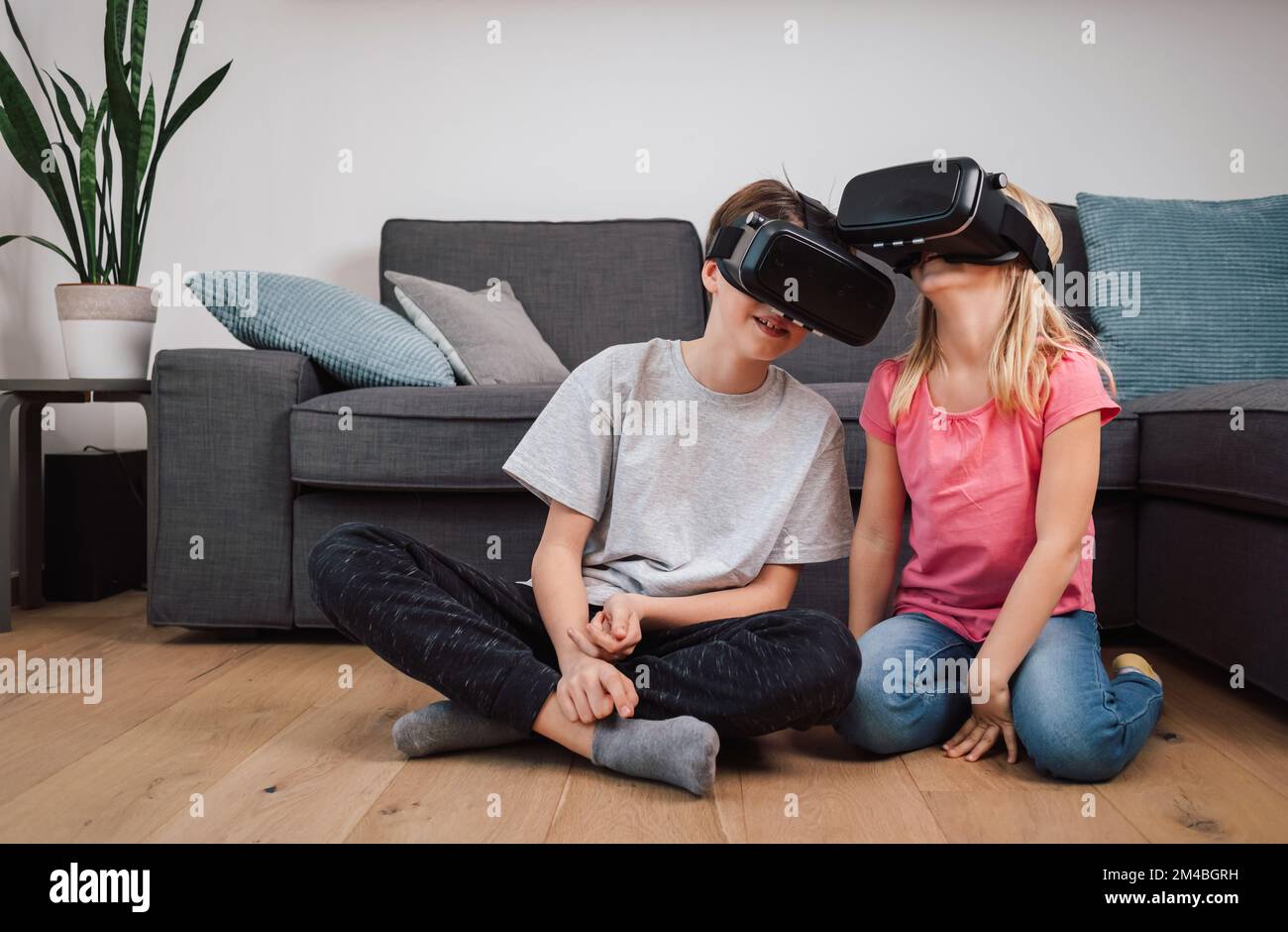 Amazed kids using virtual reality goggles playing games at home living room. Brother and sister Stock Photo