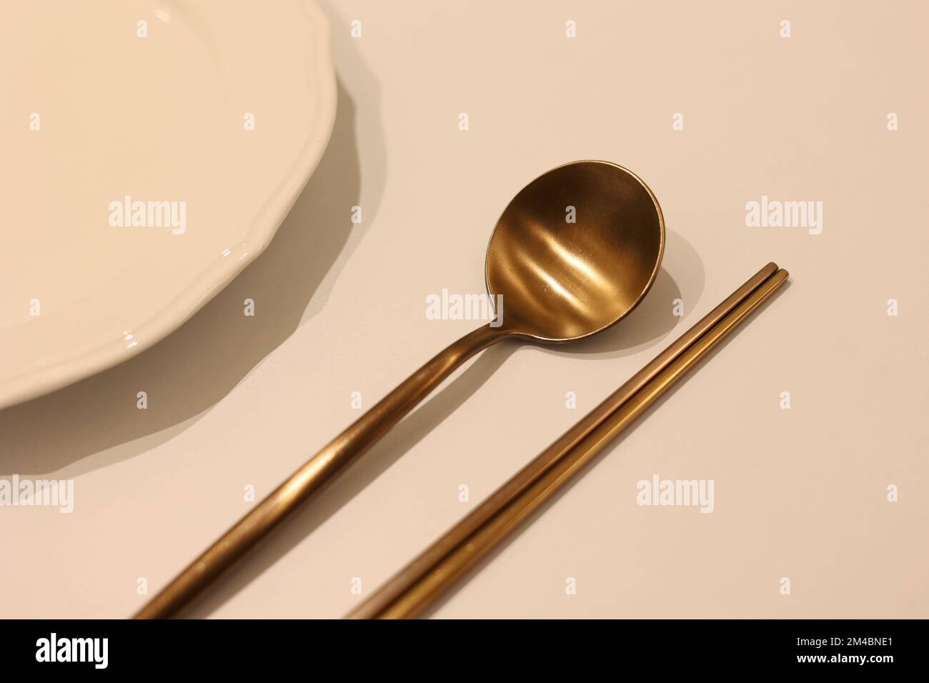 A set of Korean brass spoon and chopstick with empty white dish on the table Stock Photo