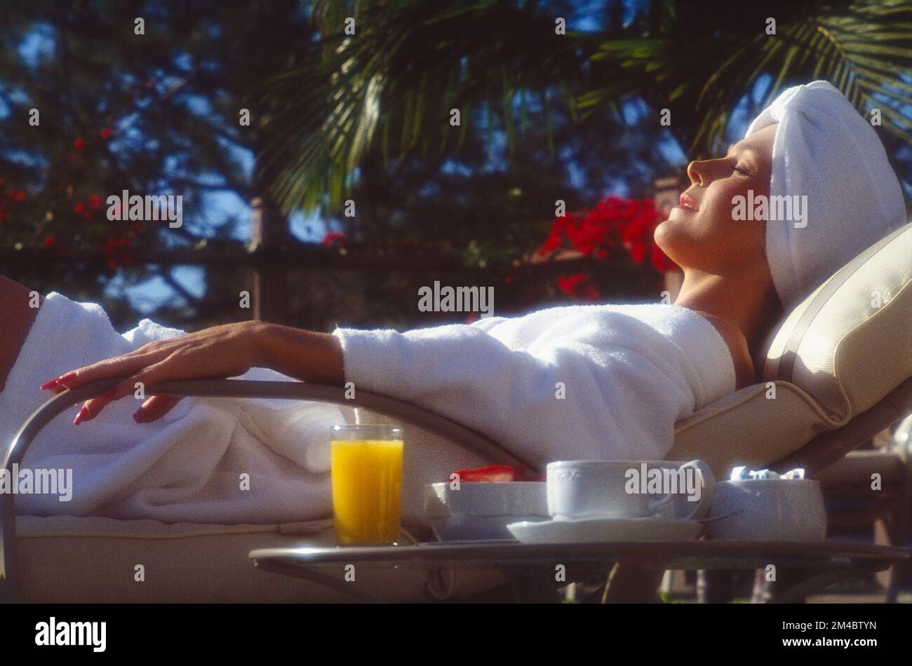 Young woman in white robe and head wrapped in a towel, lying in a lounge chair relaxing Stock Photo