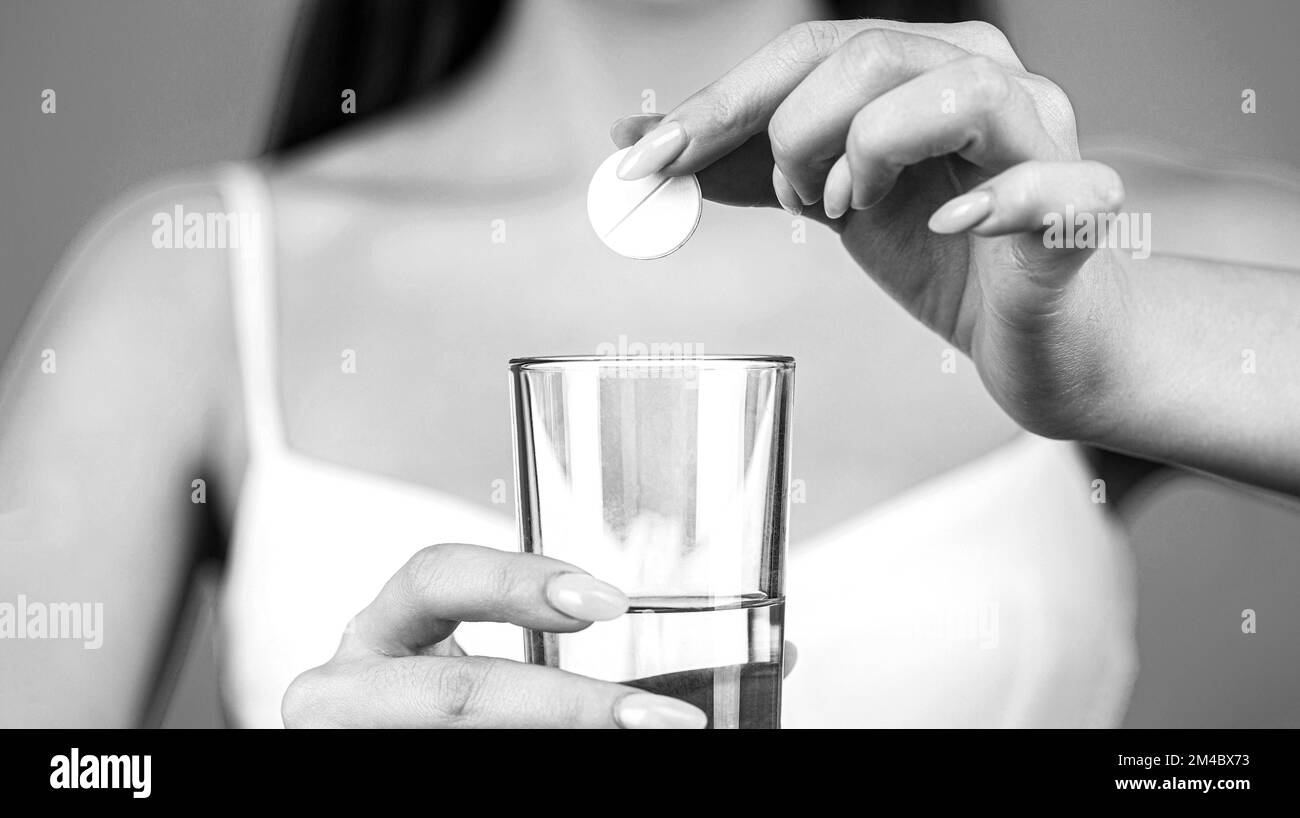 Woman taking drugs to relieve headache. Take some pills, holds glass of water. Young woman taking pill against headache. Black and white Stock Photo