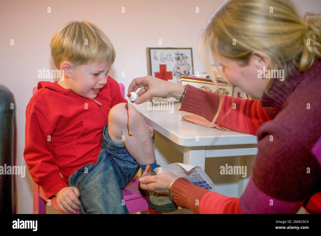 Netherlands, Arnhem; Mother puts iodine on the injured knee of her crying son. Stock Photo