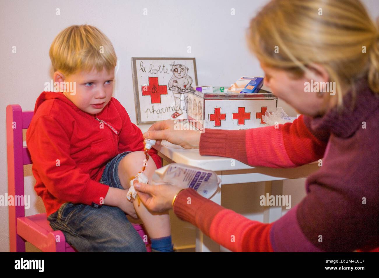 Netherlands, Arnhem; Mother puts iodine on the injured knee of her crying son. Stock Photo
