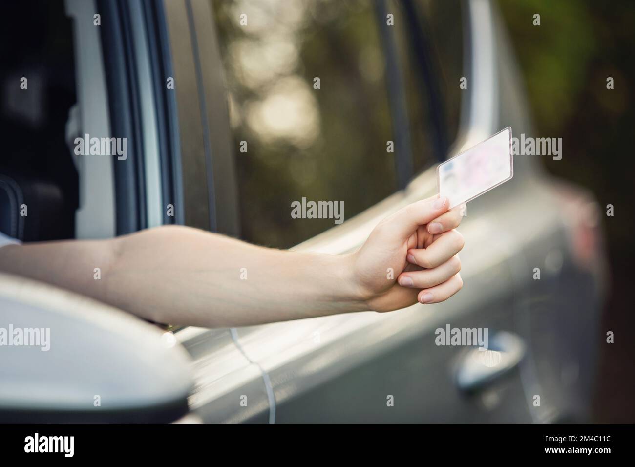 Close up person hand out of the car window holding the driver license as shows it to the police officer for control Stock Photo