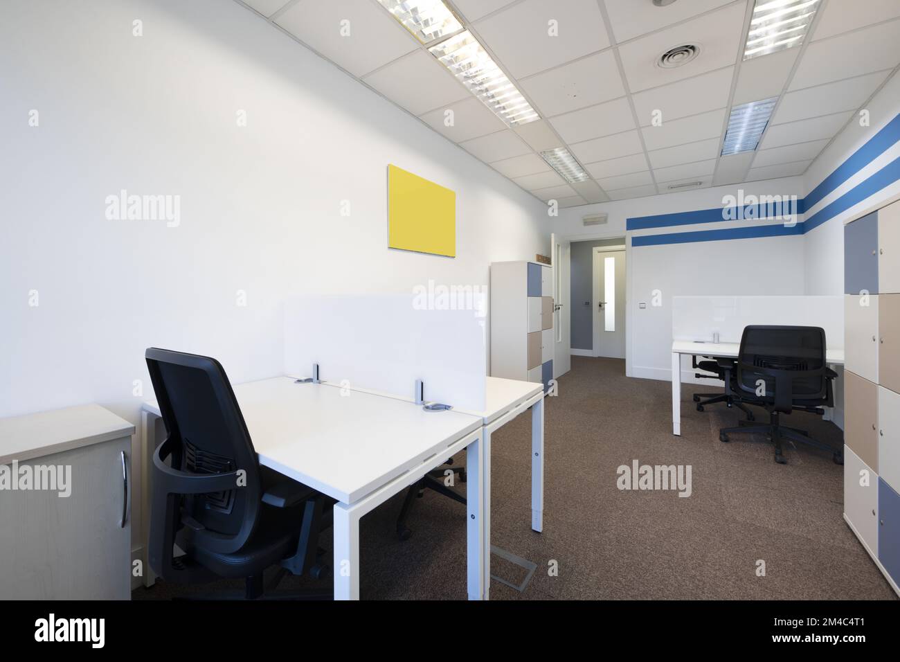 Several empty corporate work desks with divider screens and filing cabinets Stock Photo