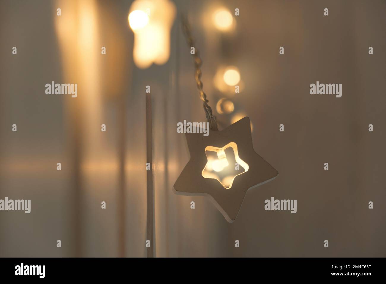 Star Shaped Christmas Lights Garland Hanging on a Wood Wall. Close Up, Selective Focus. Bedroom Interior. Cozy Home Moment. New Year's, Christmas Mood Stock Photo