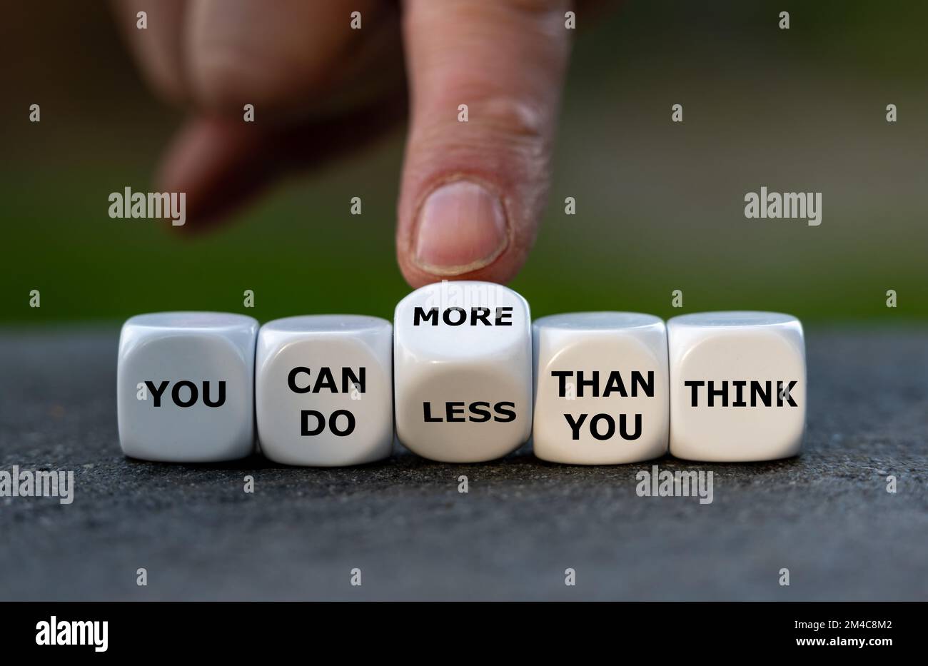 Hand turns dice and changes the expression 'you can do less than you think' to 'you can do more than you think'. Stock Photo
