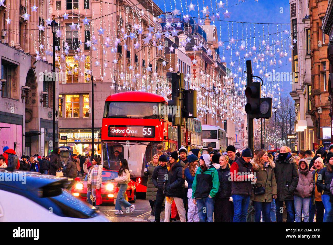 Oxford Circus, Oxford Street, London - Crowds of shoppers beneath the Christmas lights waiting to cross the road with red bus and other traffic Stock Photo