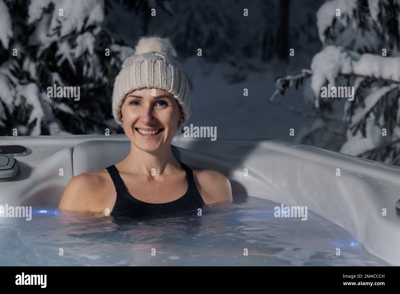 winter spa. smiling woman with knitted hat relaxing in outdoor hot tub. copy space Stock Photo