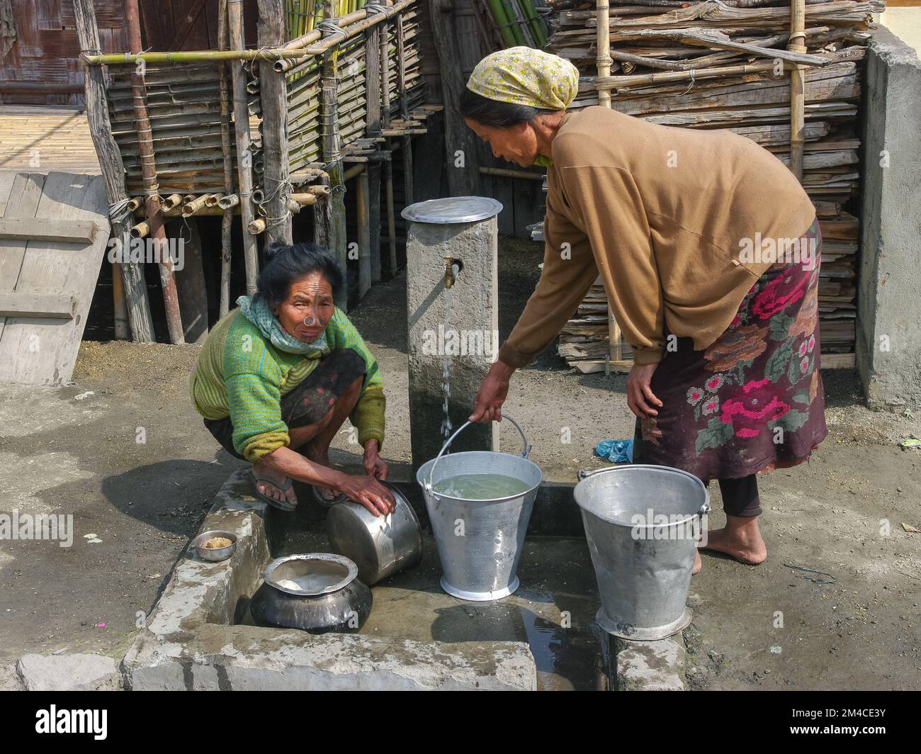 Ziro, Arunachal Pradesh, India - 03 04 2014 : Local Apatani tribal women with traditional facial tattoos and nose plugs cleaning pots at village tap Stock Photo