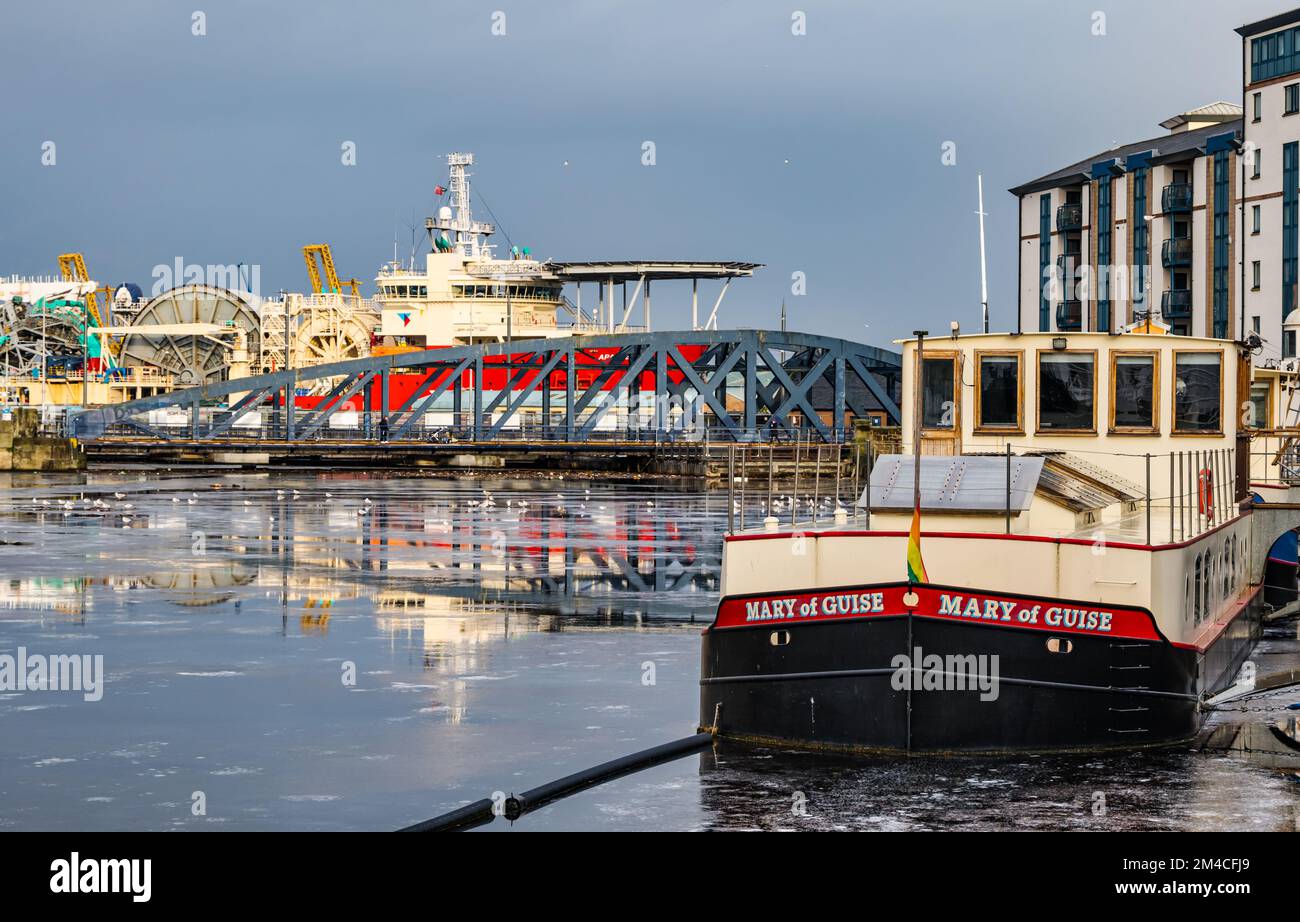 Houseboat, iron Victoria Bridge and offshore supply ship in Leith Harbour in Winter with frozen