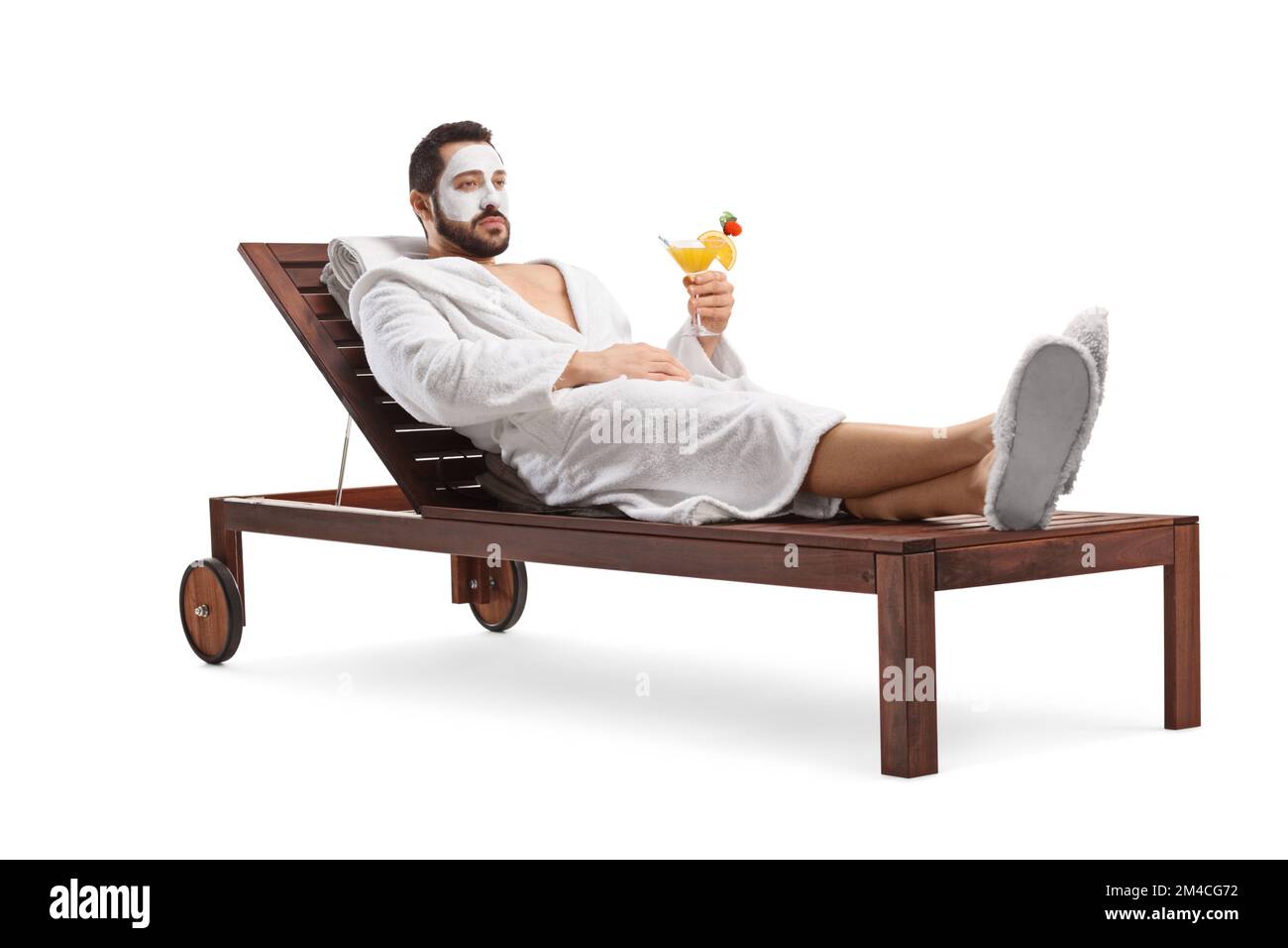 Man in a bathrobe with a face mask relaxing on a deck lounge chair with a cocktail isolated on white background Stock Photo