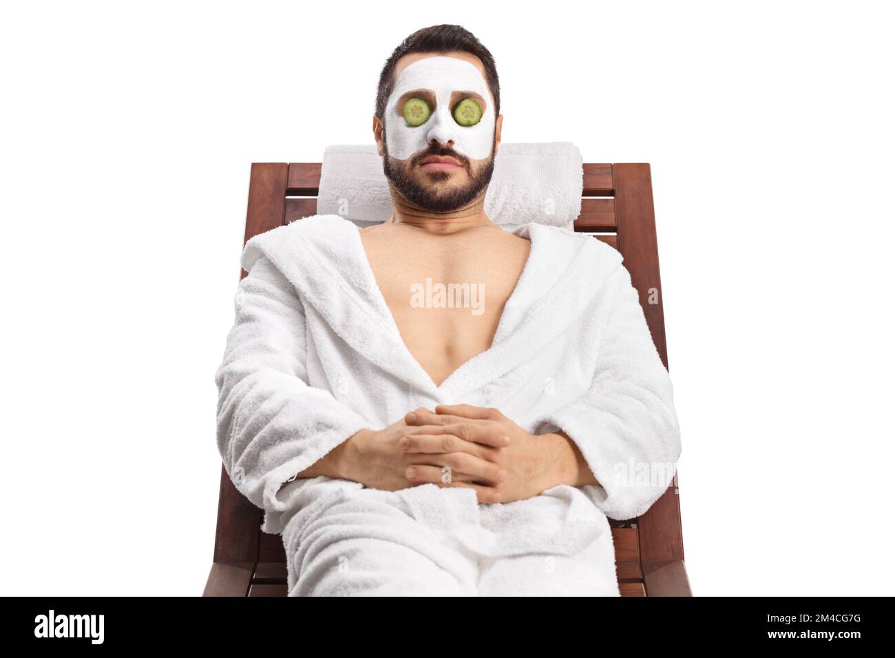 Man with a face mask and cucumber over eyes relaxing on a lounge chair isolated on white background Stock Photo