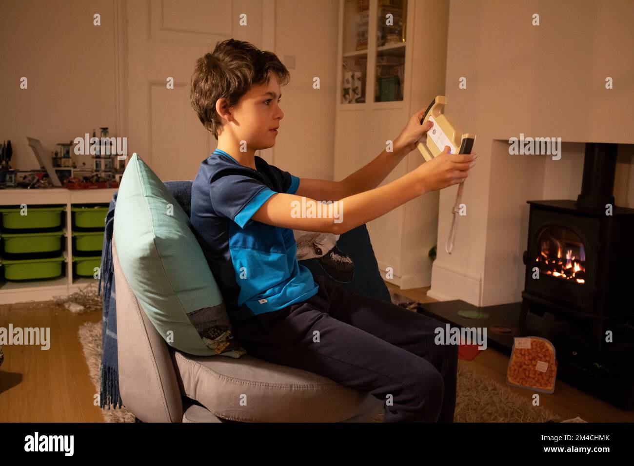 9 year old boy playing Nintendo video game at his residential home, whilst sat comfortably next to a gas fire burner, London, England, UK Stock Photo