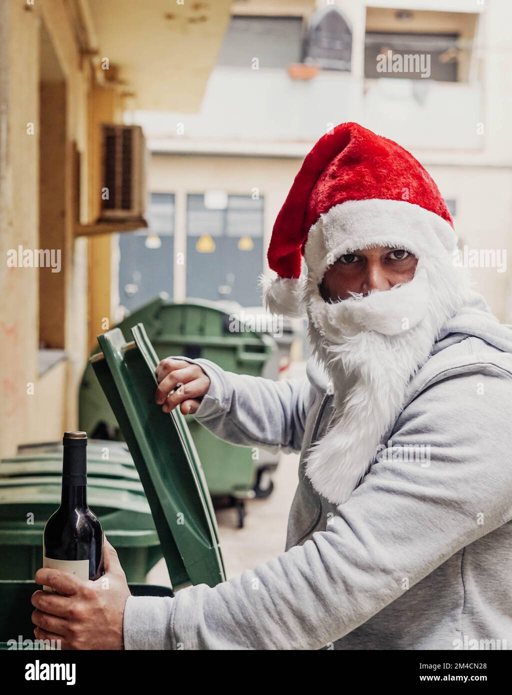 Homeless Santa drinking wine and rummaging through garbage bins Stock