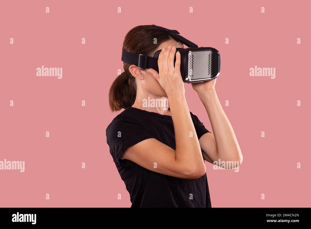 Woman wearing a virtual reality headset, pink background. Stock Photo