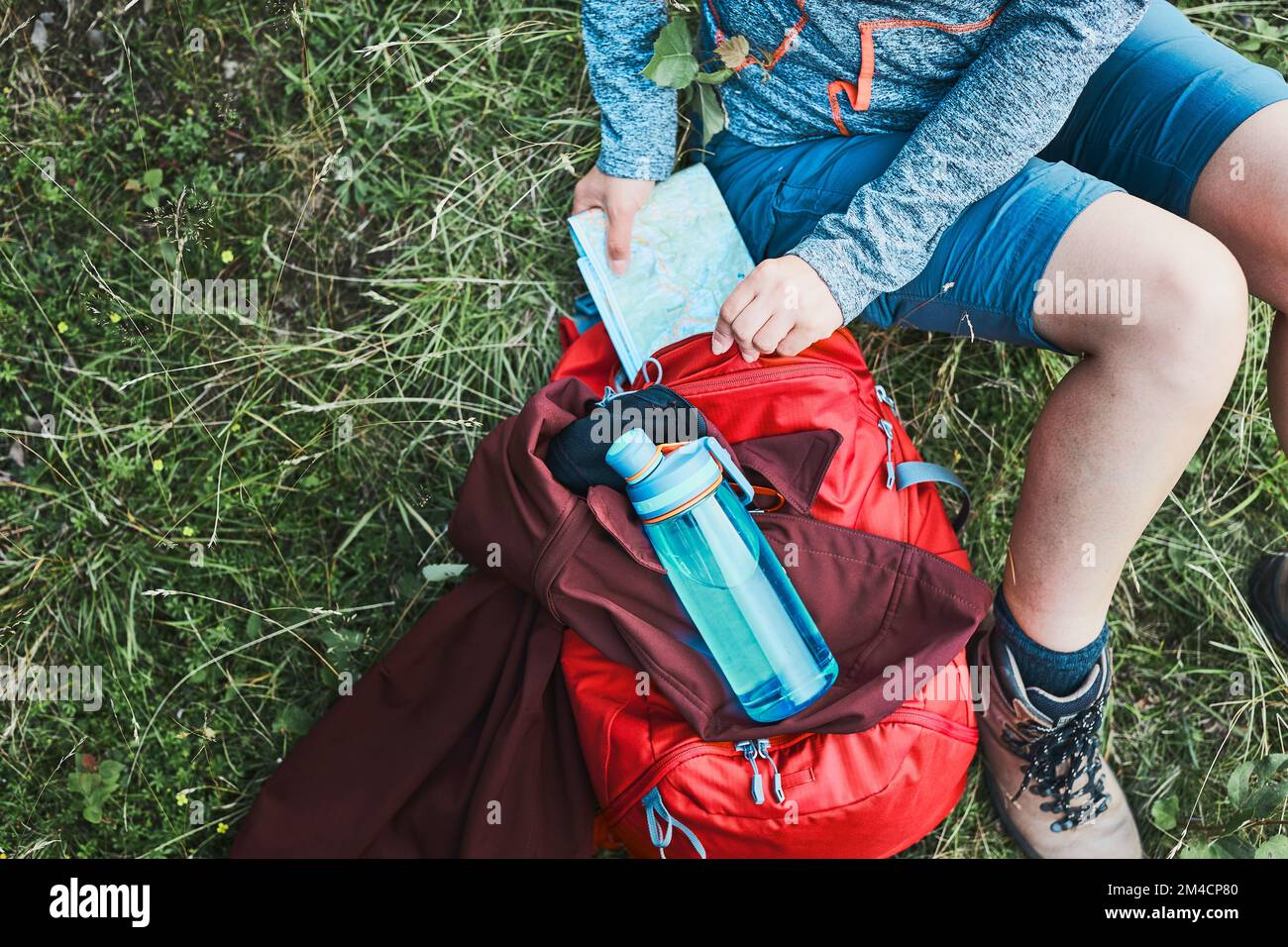 Woman with backpack having break during trip in mountains taking map out sitting on grass on summer vacation day Stock Photo