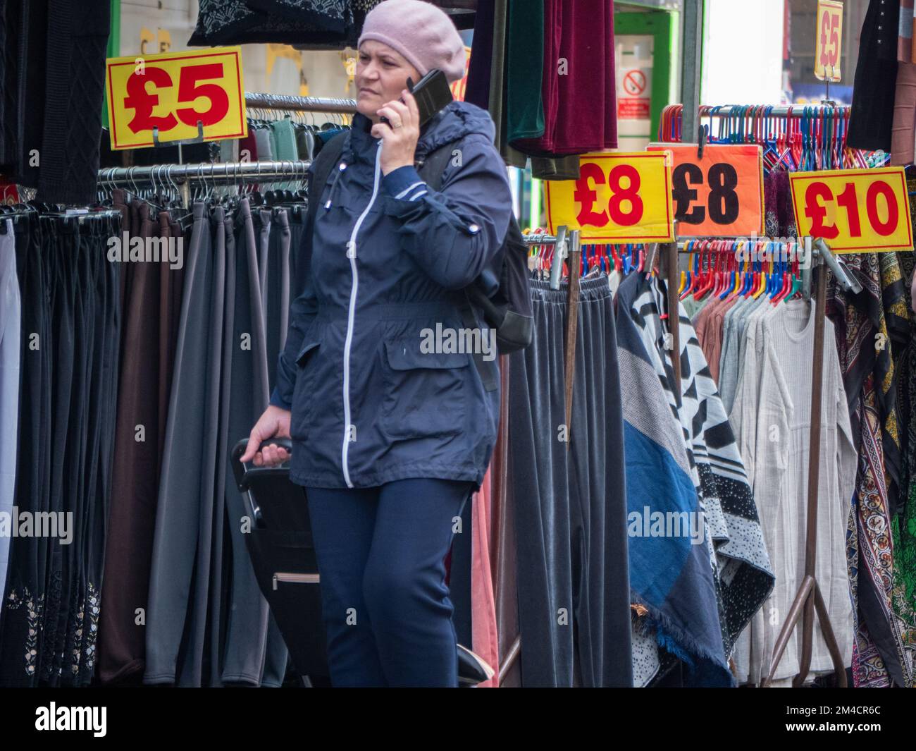 Shopper walks past goods in Walthamstow market, London, UK, the longest outdoor market in Europe. Traders and market stall holders serve shoppers, with prices displayed in pounds Stock Photo