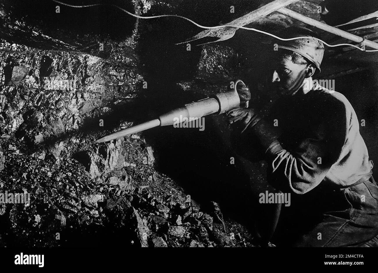 Coal miner / hewer working underground in shaft, extracting coal by hand with pneumatic hammer / pick in colliery / coal mine / coal pit Stock Photo