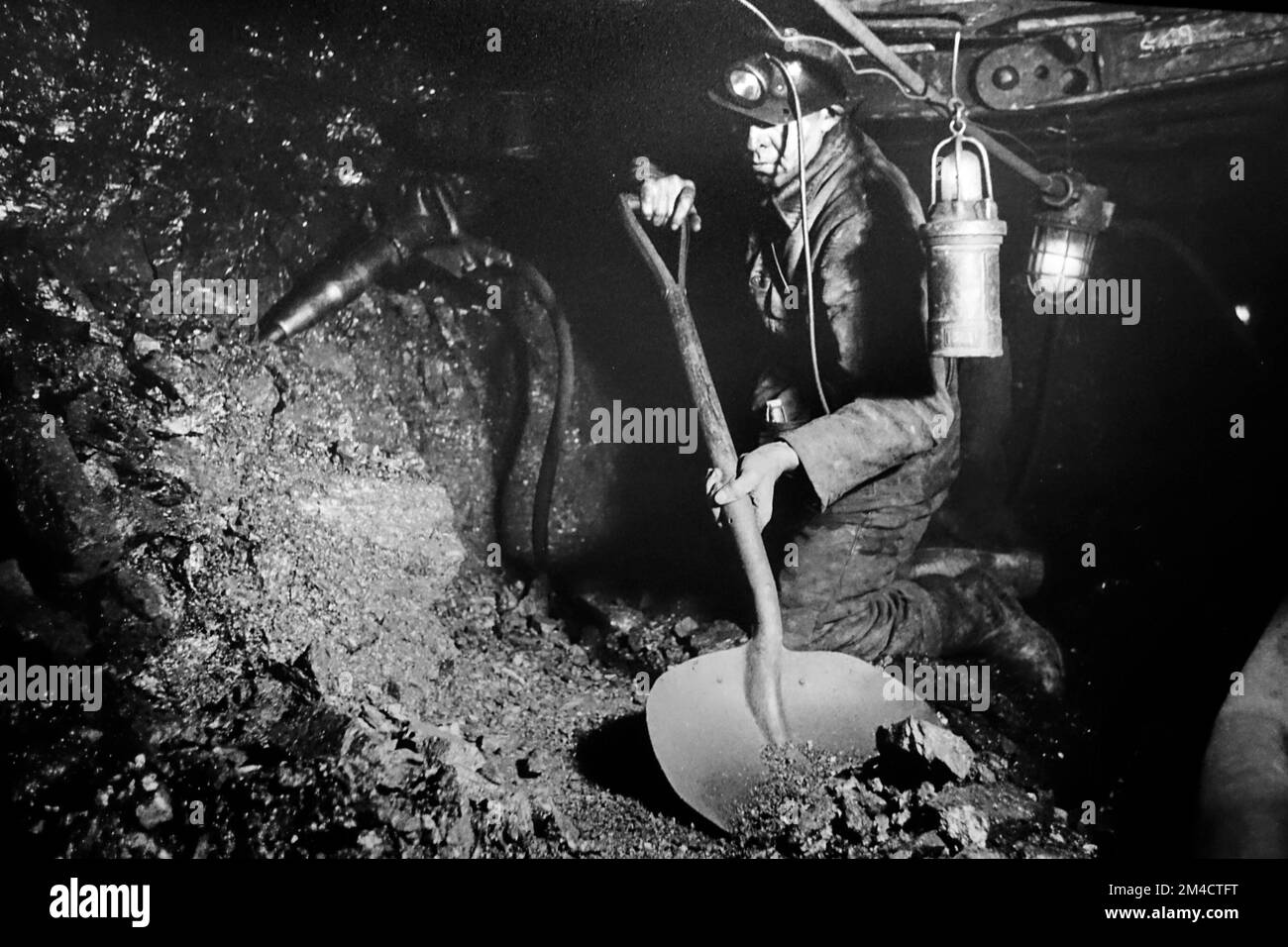 Coal miner / hewer working underground in shaft, extracting coal by hand with shovel and pneumatic hammer / pick in colliery / coal mine / coal pit Stock Photo