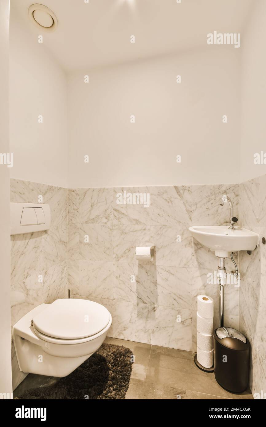 a modern bathroom with marble walls and flooring, including a white toilet and black rug in the corner of the room Stock Photo