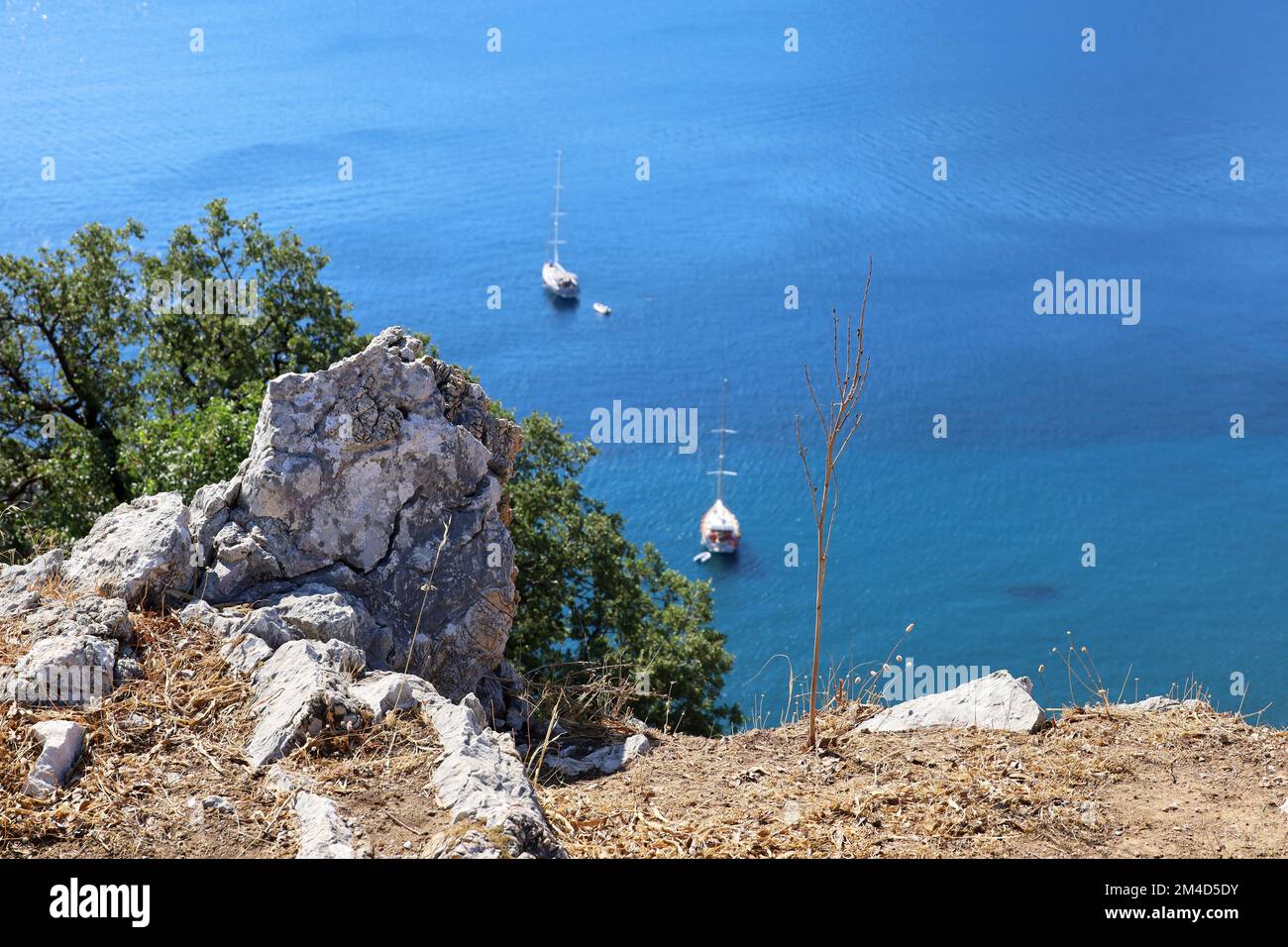 Defocused view from the top of a mountain to blue sea with sailing yachts, focus on a rock. Travel and vacation on Mediterranean islands Stock Photo