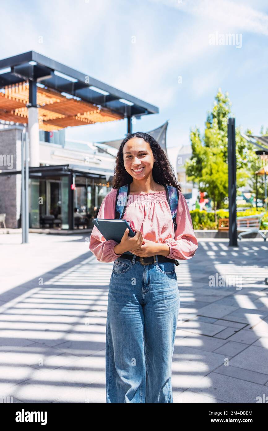 Confidence. Smiling latin university student woman standing and holding her books outside of the campus  Stock Photo