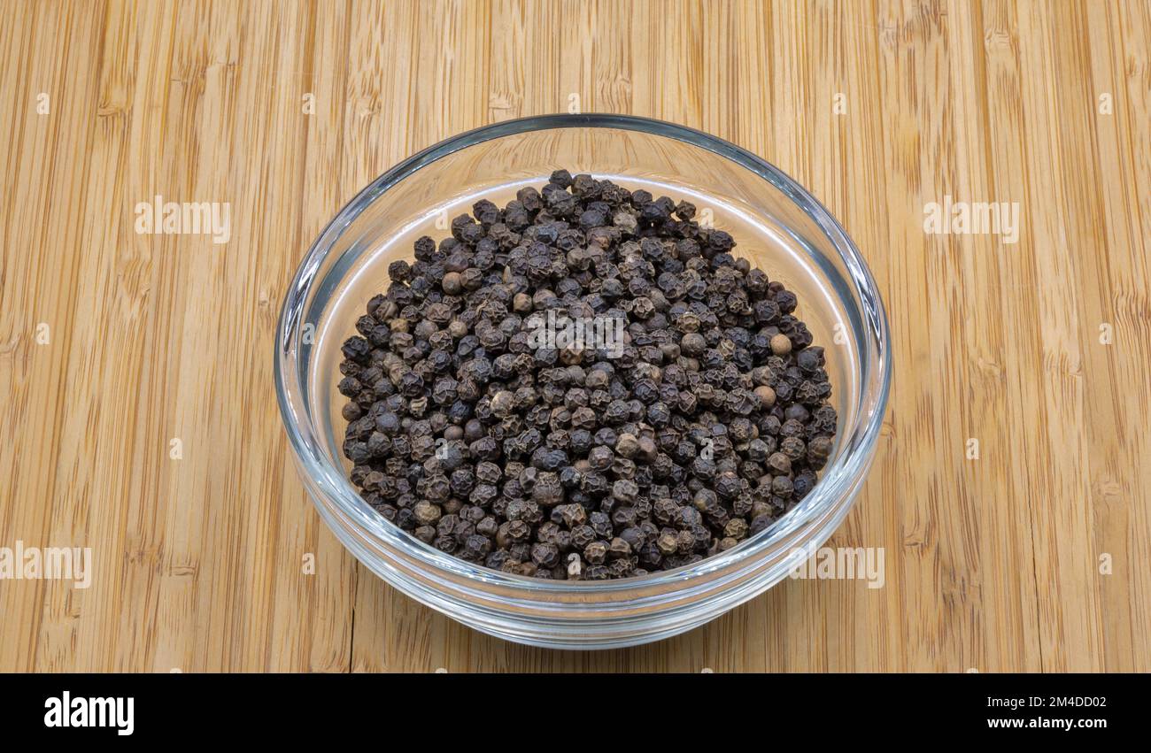 Black pepper in a glass bowl closeup on wooden background Stock Photo