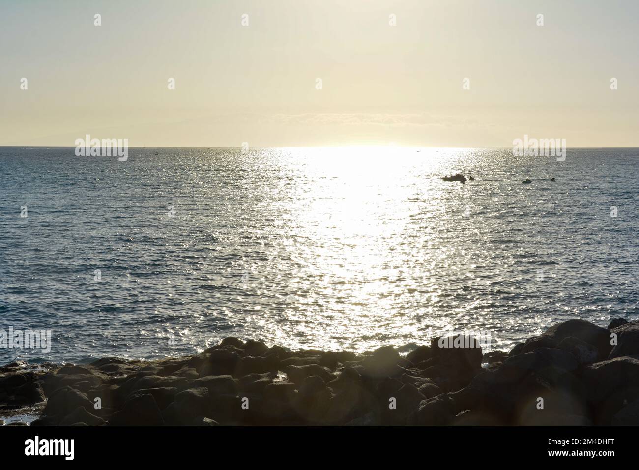 Boats on the sea with reflections of the sun at sunset, large stones in ...