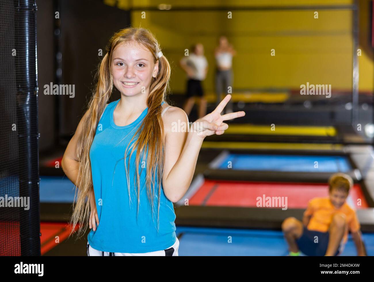 Cheerful teen girl giving V sign in indoor trampoline arena Stock Photo ...