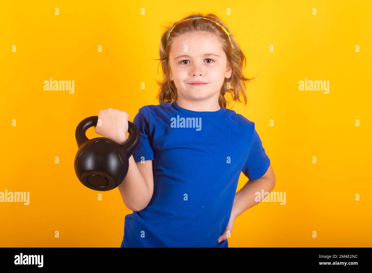 Cute child boy pumping up arm muscles with kettlebell dumbbell. Fitness kids with dumbbells. Stock Photo