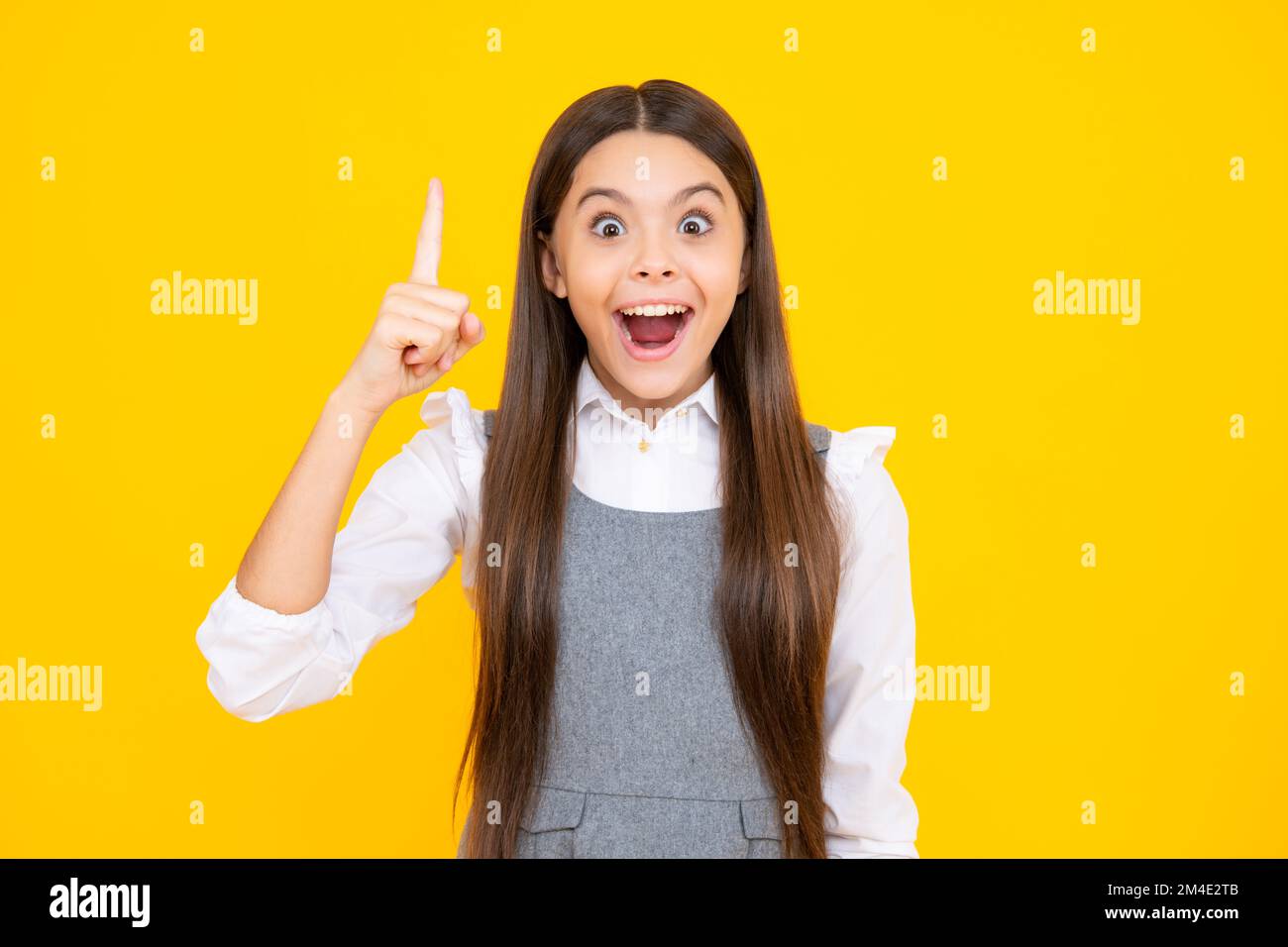 Excited face. Young teenager pointing up with finger, isolated on yellow background. Girl has great new idea. Funny school girl, kid genius, nerd Stock Photo