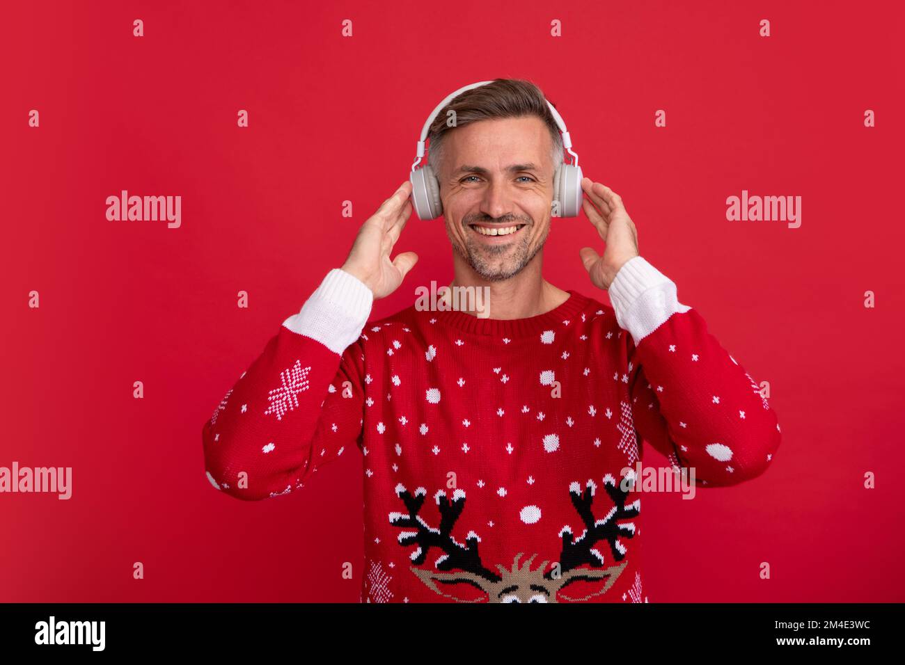 Christmas music. Santa with headphone. Portrait of middle aged man in sweater isolated over red background. Concept of holidays, happiness, emotions Stock Photo