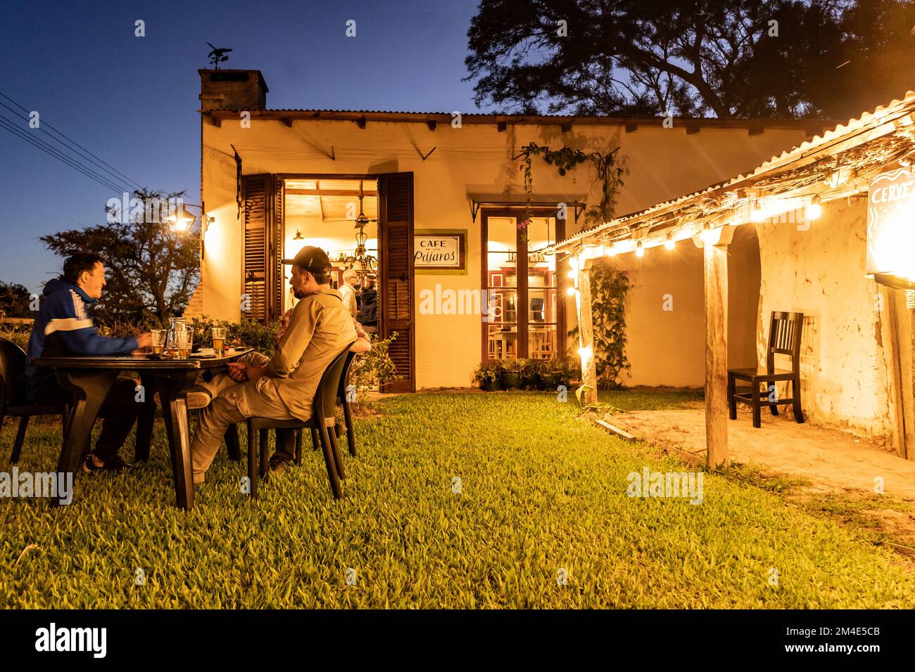 COLONIA CARLOS PELLEGRINI, CORRIENTES, ARGENTINA - NOVEMBER 20, 2021: A group of people enjoy a beer in the garden of a rustic small pub next to Cafe Stock Photo