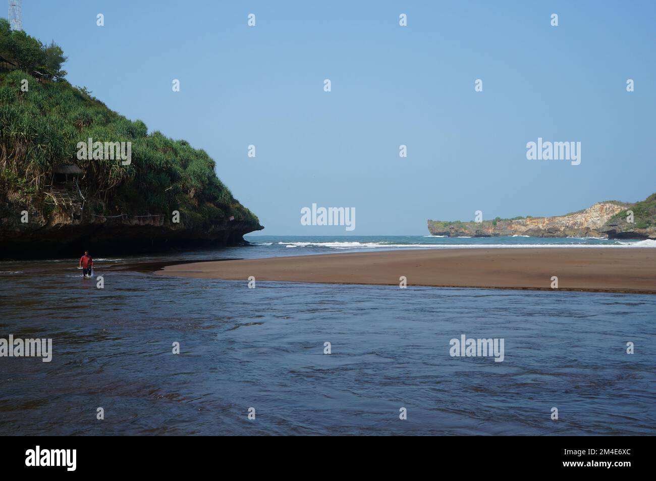 The beautiful sea beach in Yogyakarta is surrounded by rocky hills. Someone walking on water Stock Photo