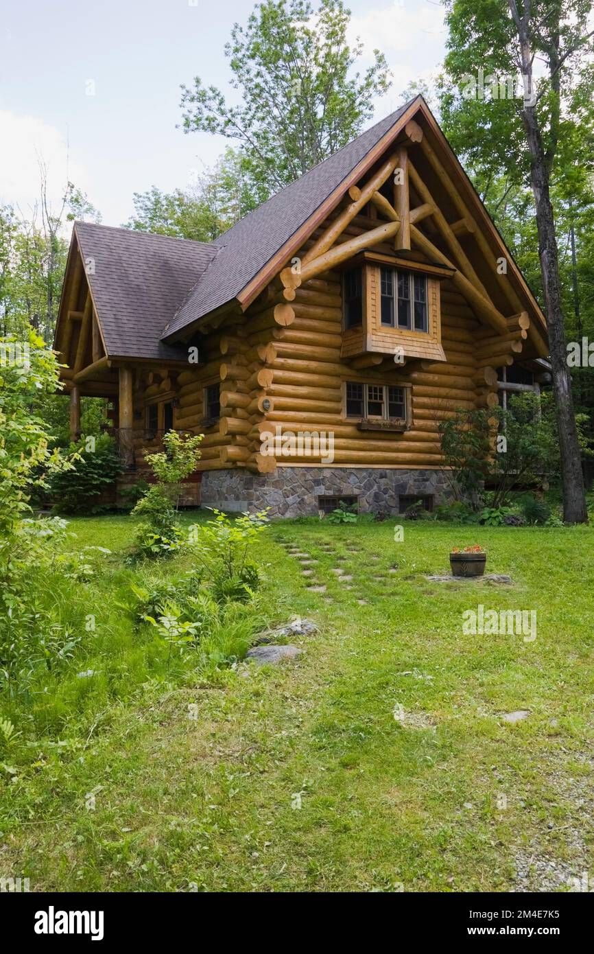 2003 built cottage style log home with brown asphalt shingles roof and natural stone foundation in spring. Stock Photo