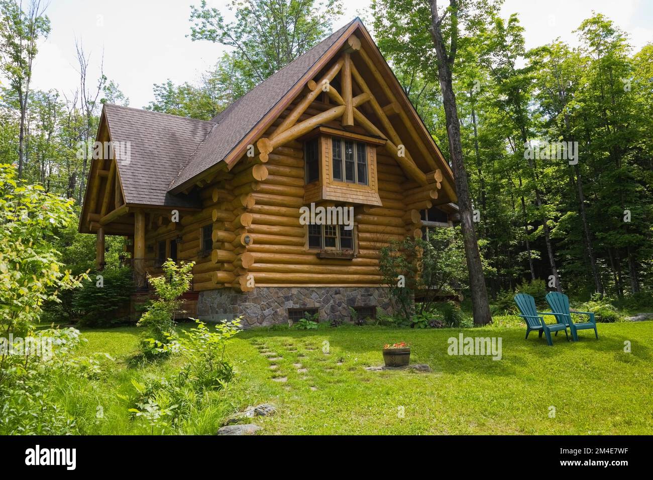 2003 built cottage style log home with brown asphalt shingles roof and natural stone foundation in spring. Stock Photo