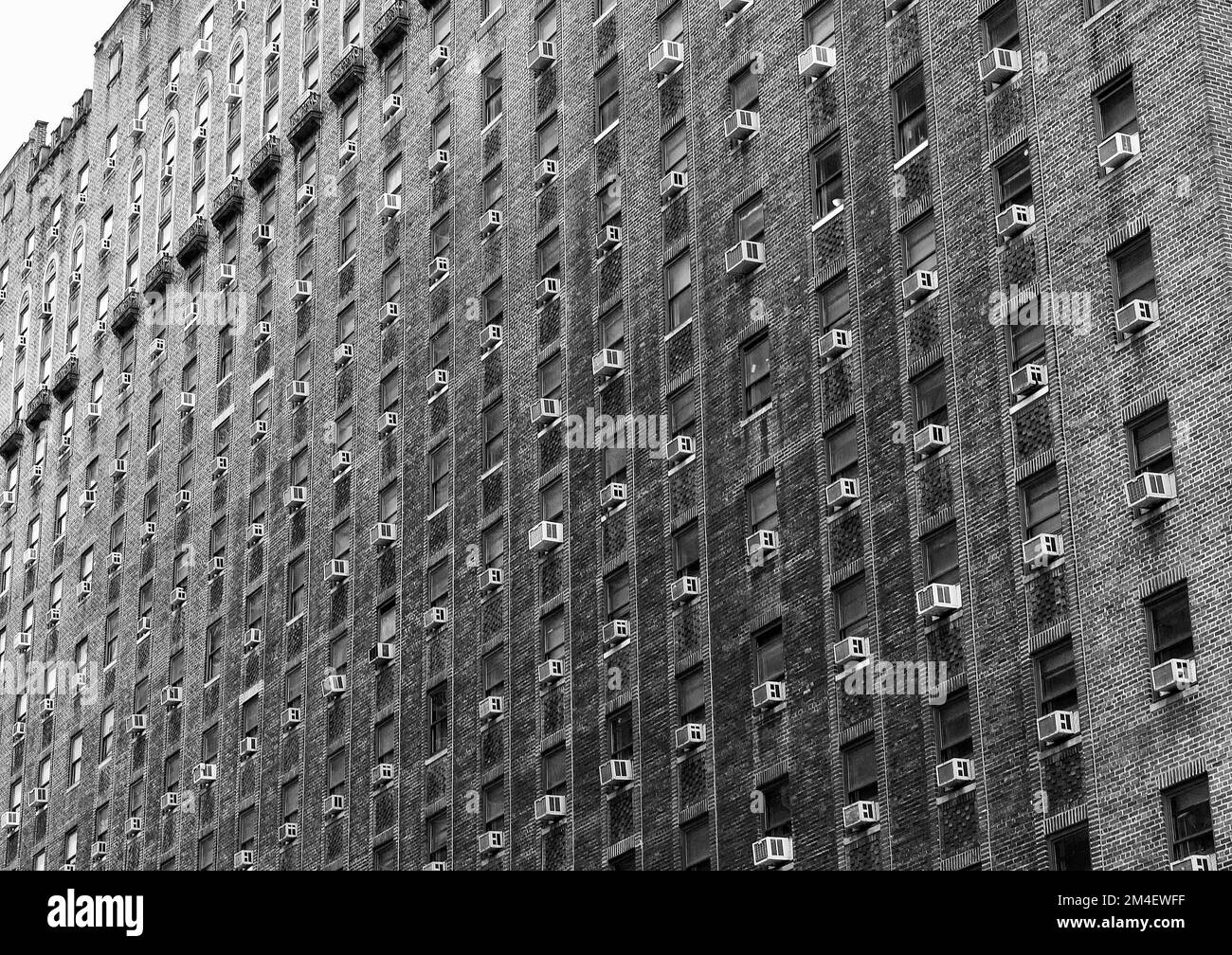 A low-angle shot of a big building covered in similar windows with air conditioning units in greyscale Stock Photo