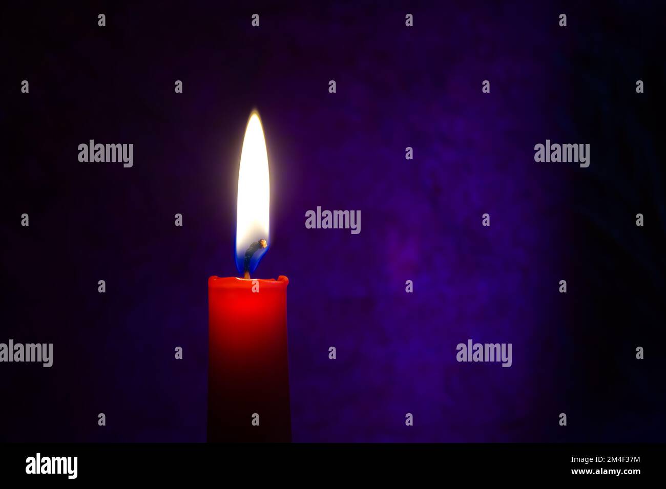 Single red candle burning alone in the dark blue background. Conceptual