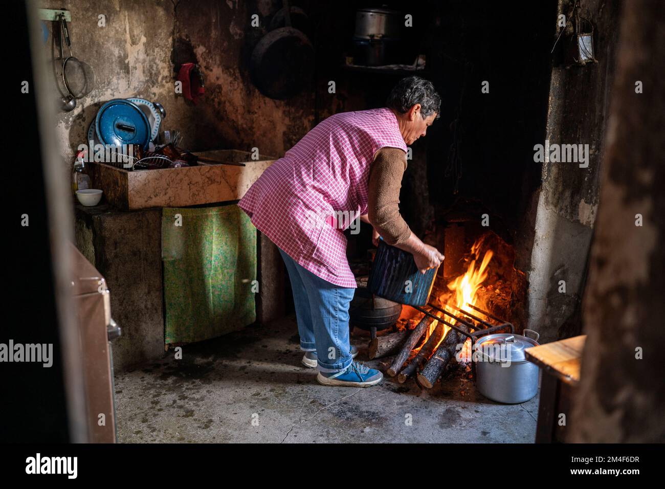 Woman cooking on open fire in a small old-fashioned kitchen in a country house Stock Photo