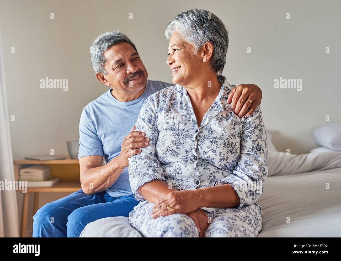 Our lives are the adventure weve been living for. Portrait of a cheerful mature couple holding each other while being seated on a bed at home during Stock Photo