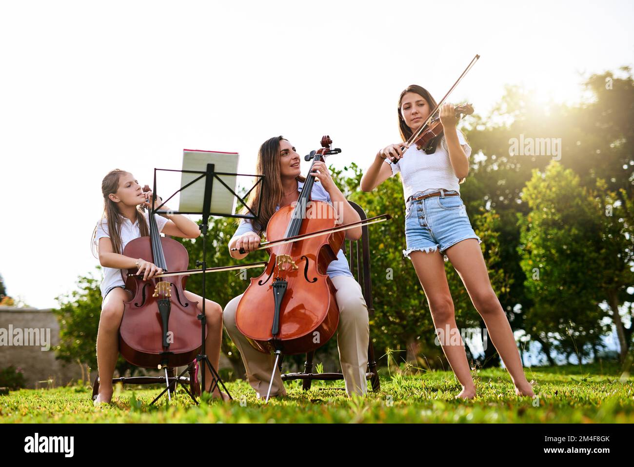 We are getting better and better. a cheerful young mother and her two daughters playing classical string instruments together while standing in the Stock Photo