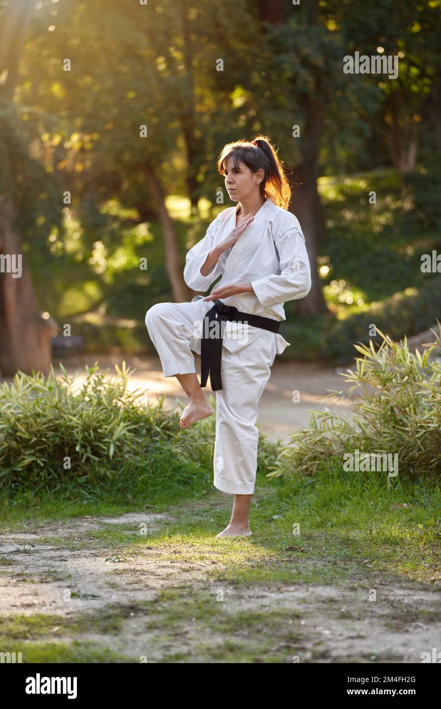 Woman in kimono and black belt standing in pose while practicing karate outdoors in nature. Sports and martial arts concept. Stock Photo