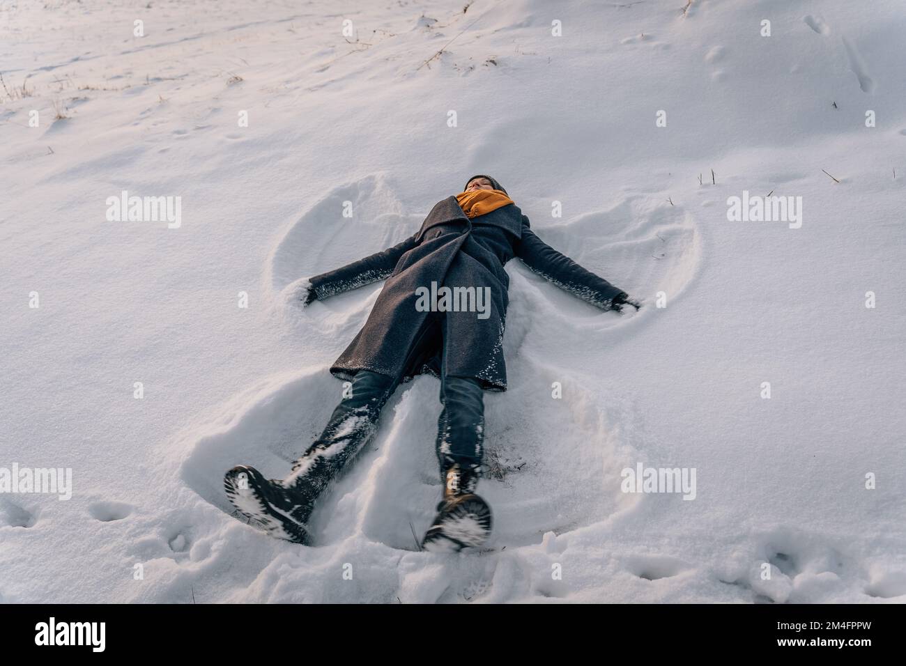 A woman lies in the snow in the shape of a snow angel in winter Stock Photo
