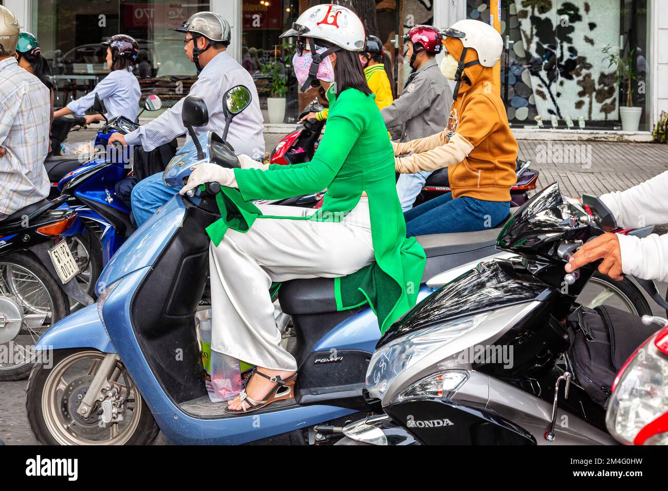 Lady riding scooter, in traditional Ao Dai, wearing safety helmet, in traffic jam, Ho Chi Minh