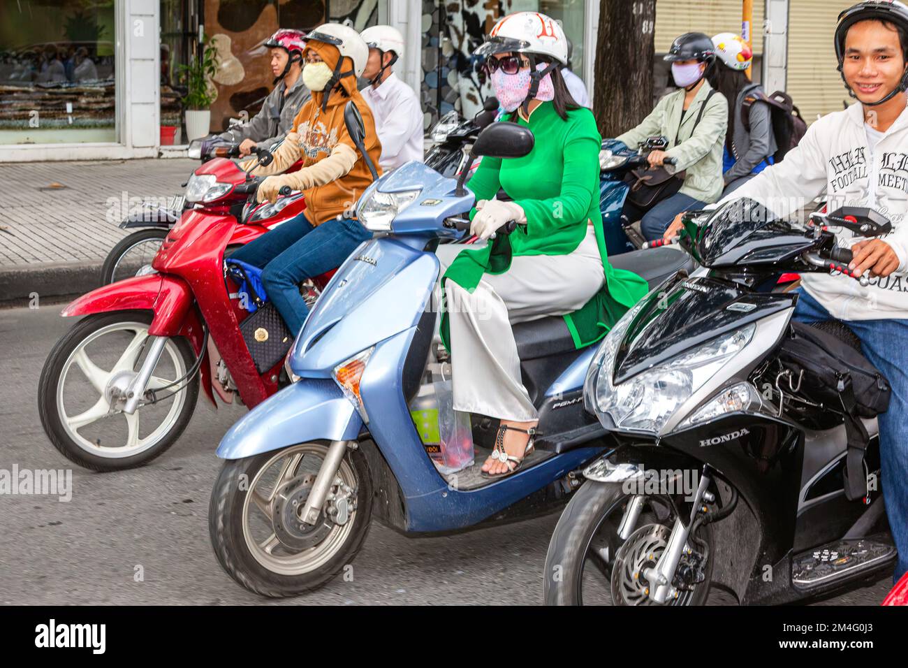 Lady riding scooter, in traditional Ao Dai, wearing safety helmet, in traffic jam, Ho Chi Minh
