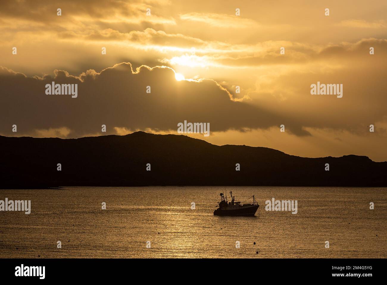 Schull, West Cork, Ireland. 21st Dec, 2022. The sun rises from behind clouds over moored fishing trawler 'Laetitia' in Schull Harbour on the shortest day of the year. Credit: AG News/Alamy Live News Stock Photo