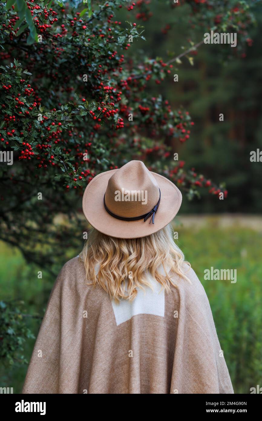 Woman with hat and poncho standing under hawthorn tree in autumn nature. Hippie fashion style Stock Photo