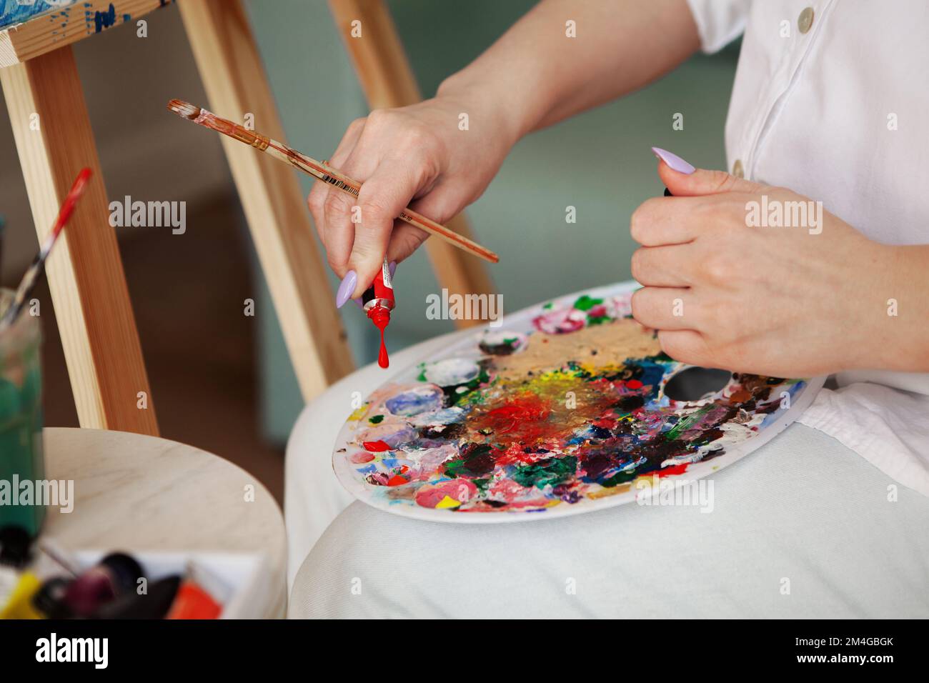 Artist hands squeeze paint out of tube on colorful palette, woman