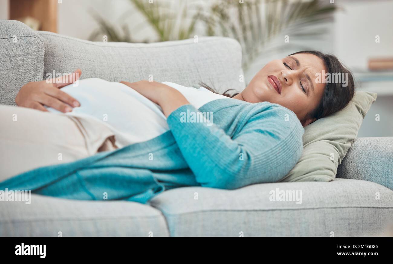 Pregnancy, cramps and woman with stomach pain on sofa holding abdomen in pain, discomfort and physical strain. Healthcare, baby and pregnant woman Stock Photo