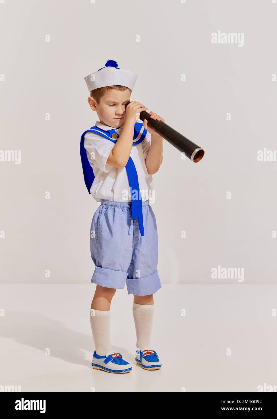 Portrait of little boy, child in image of seaman in vest posing with spyglass over grey background. Curious kid Stock Photo